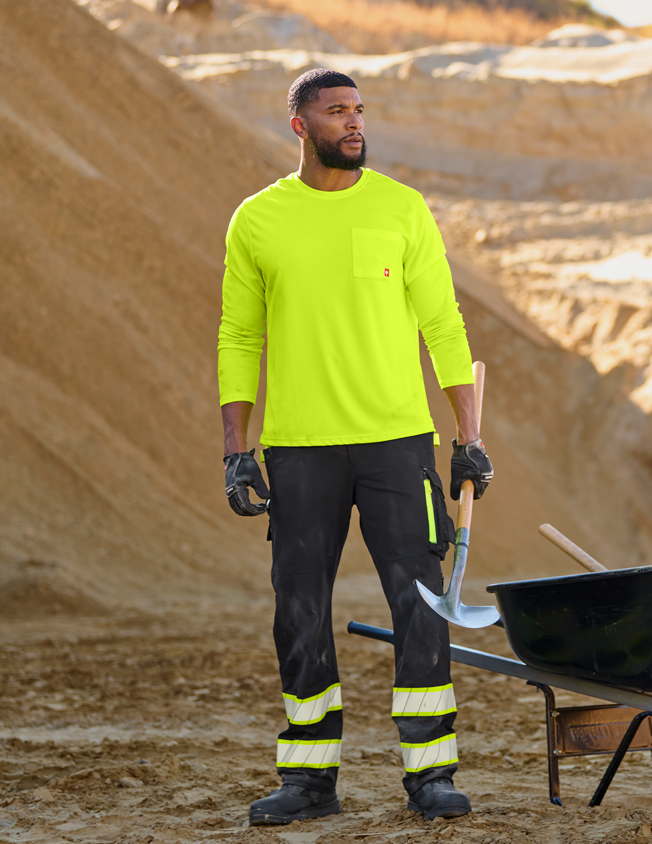 Person wearing a bright yellow long-sleeve shirt and black pants with reflective stripes, standing in a construction site.