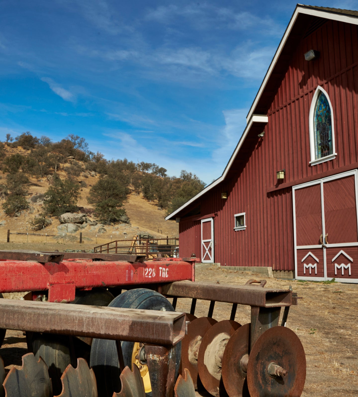 Red barn on a ranch property with dry hills rising behind it under a clear sky.