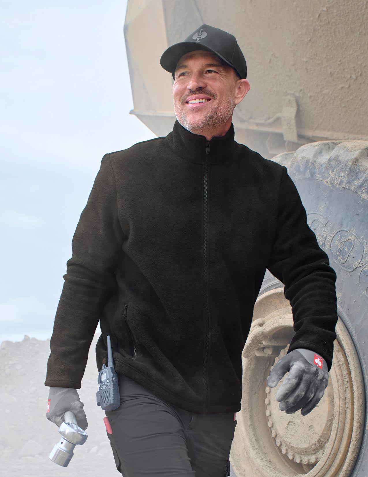 Man in black jacket and gloves standing in front of a large mechanical structure.
