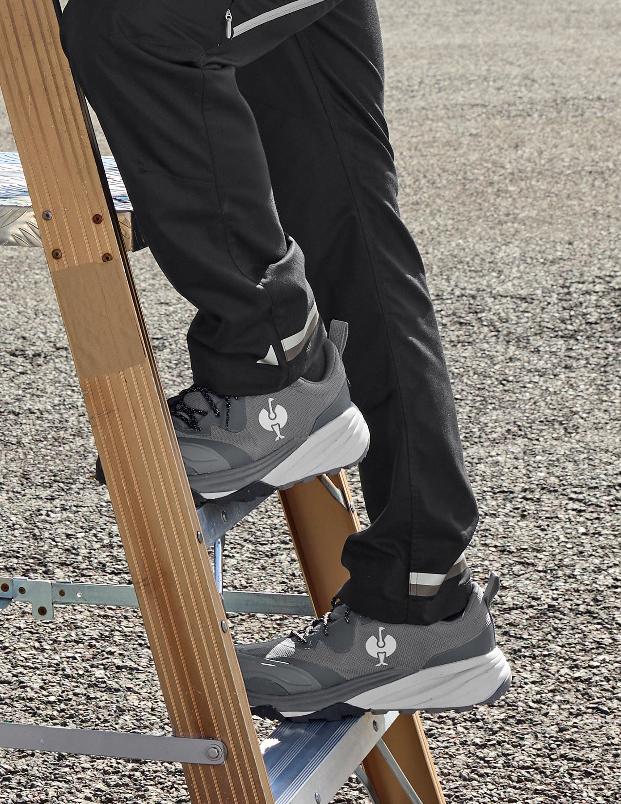 Person climbing a ladder wearing black pants and gray shoes with a STRAUSS logo.