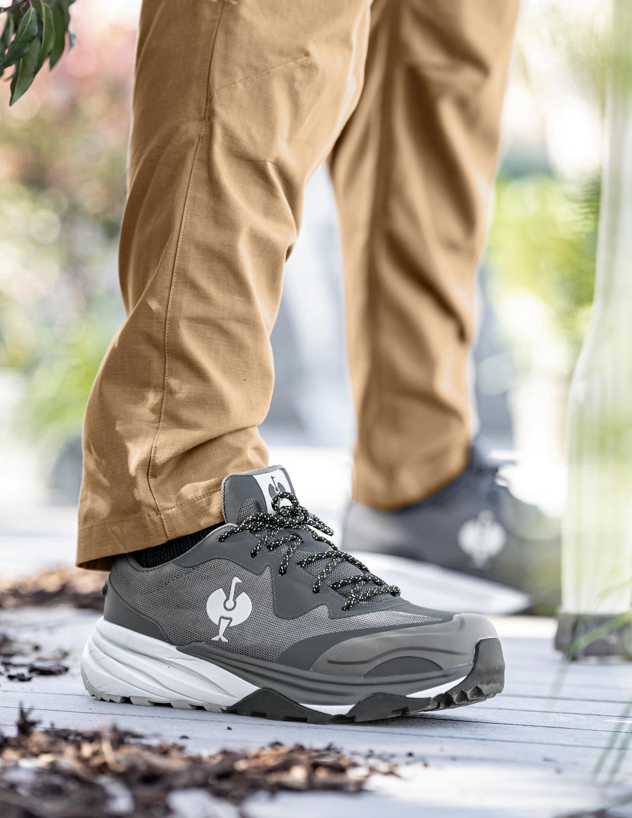 Gray hiking shoe with white sole worn by a person on a wooden deck.