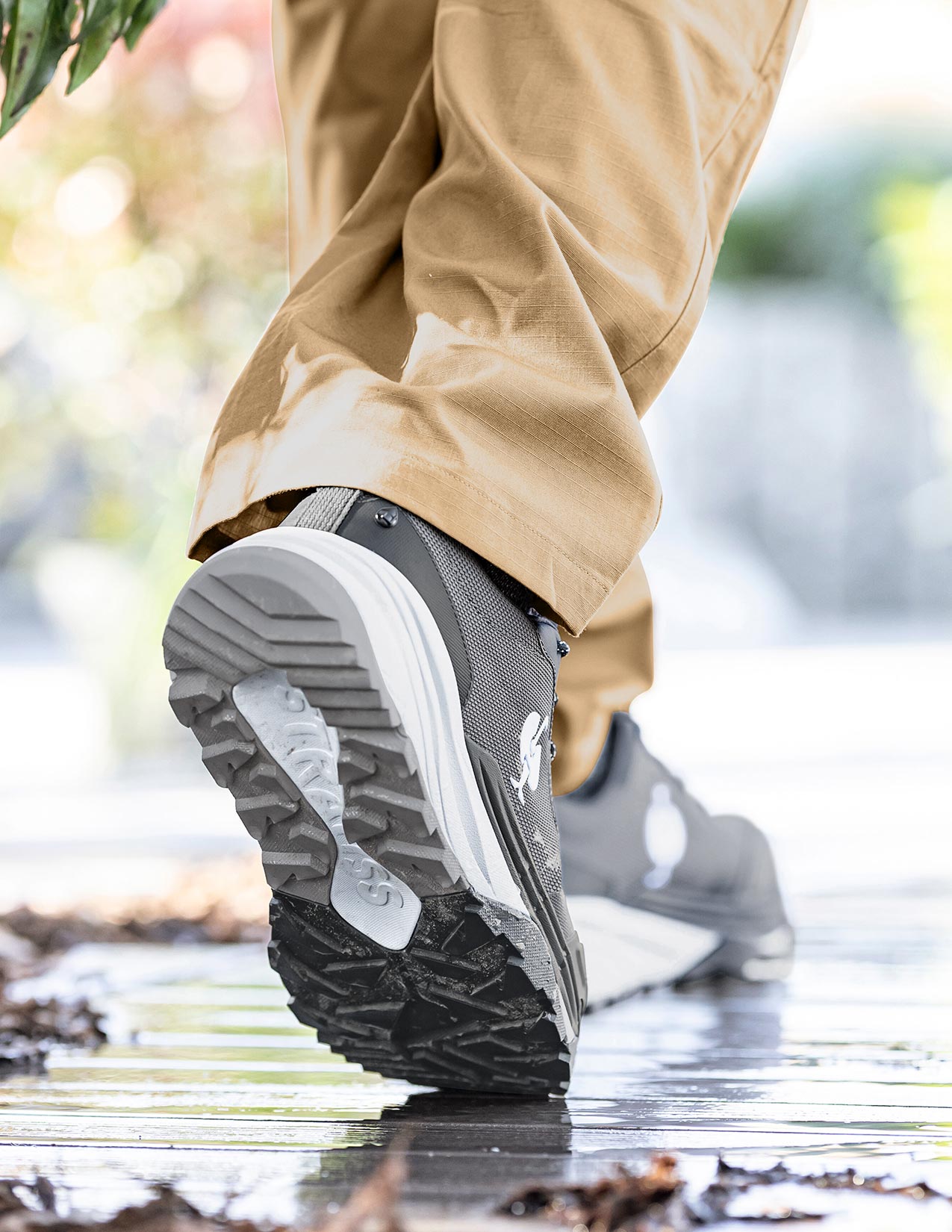Person wearing grey shoes with white soles walking on a wet surface.