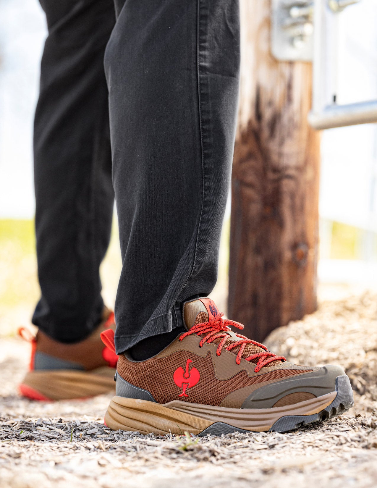 Brown hiking shoes with red laces and a red STRAUSS logo worn by a person on a natural background.
