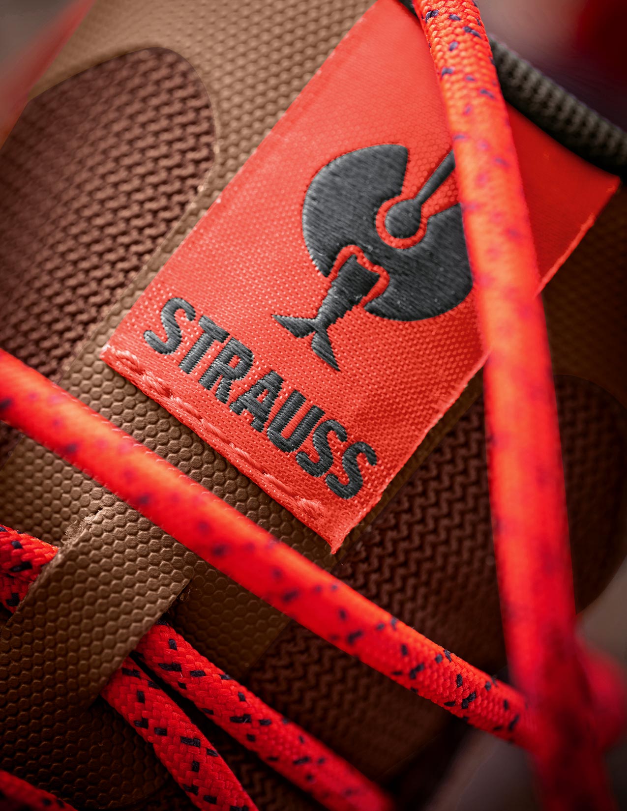 Close-up of a brown shoe with red laces and a visible 'Strauss' logo.