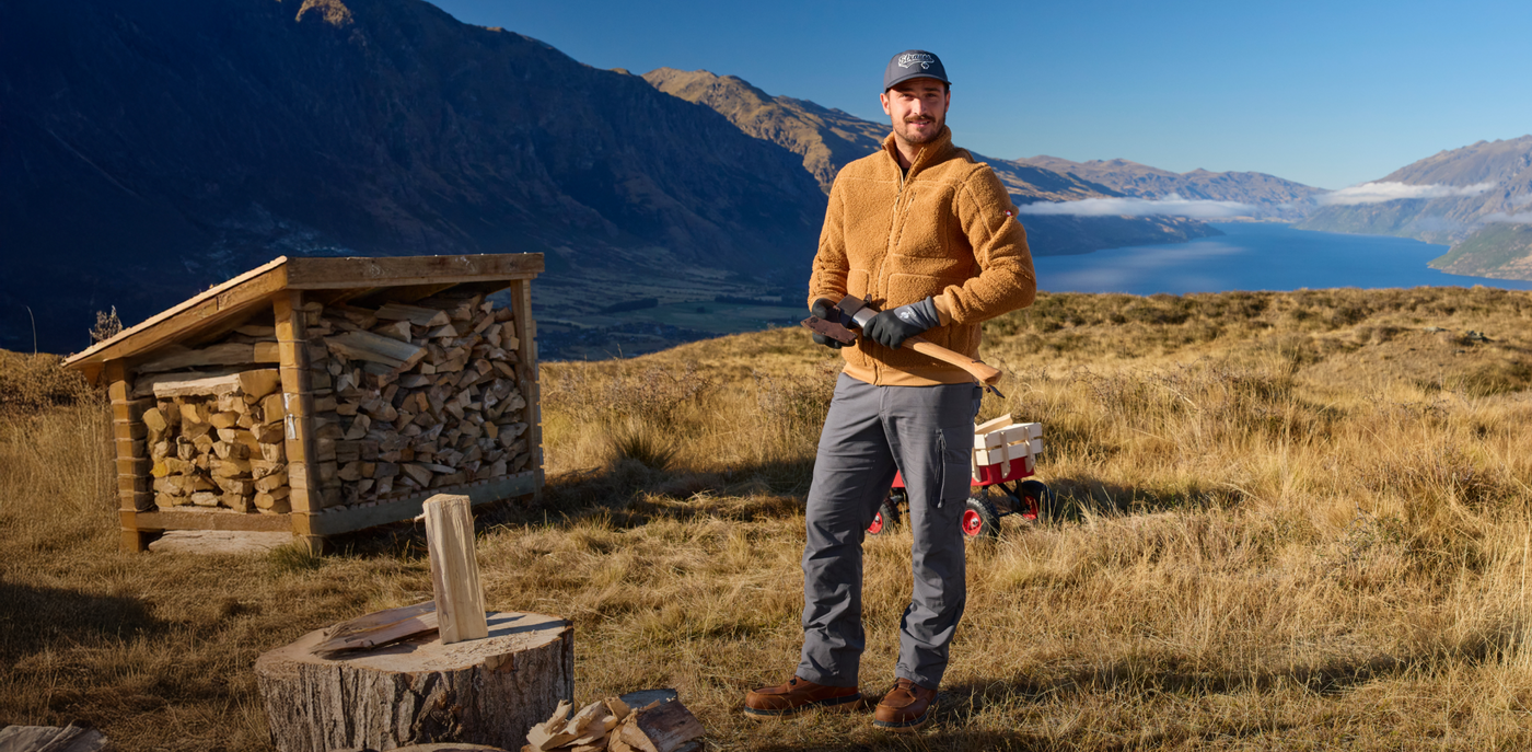 Man standing in a mountainous landscape with a wooden shed and mountains in the background