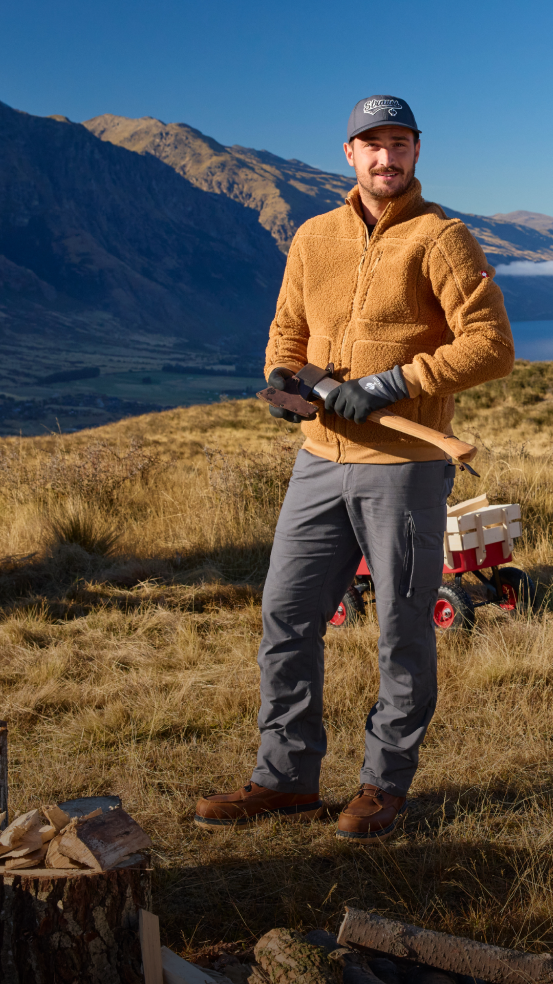 Man in brown sherpa jacket stands with mountains in the background