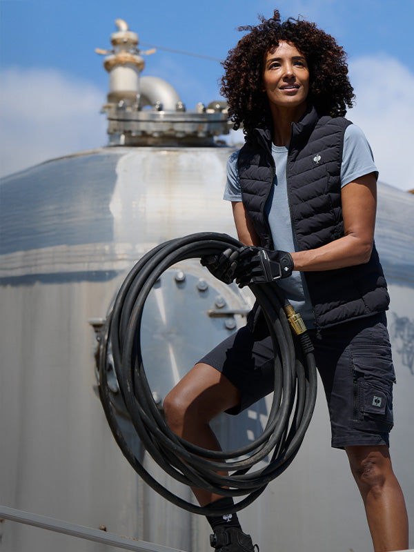 A woman holds a hose while wearing a STRAUSS vest, e.s.Motion Ten Shorts and Gloves.