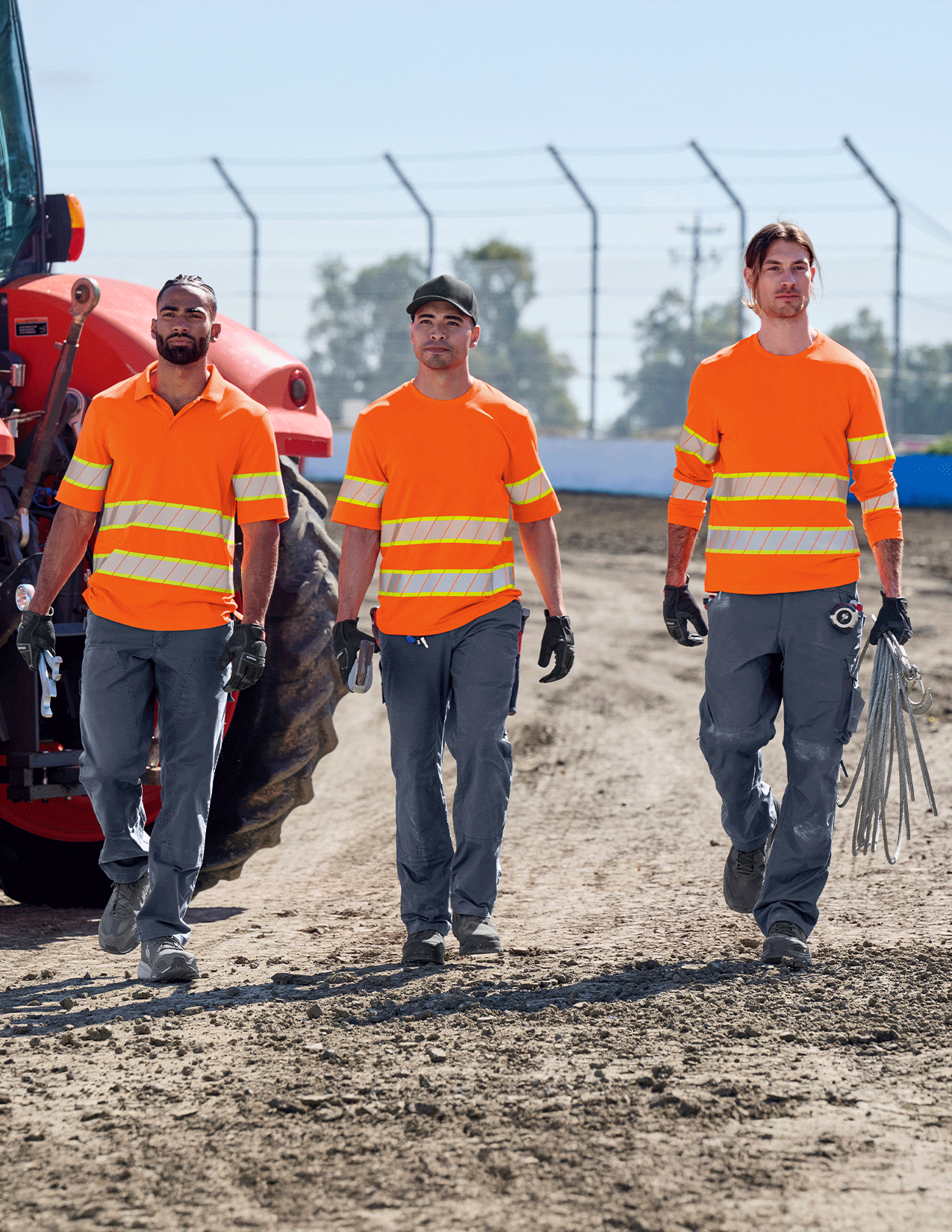 Three workers in high-visibility neon orange shirts walking on a construction site.