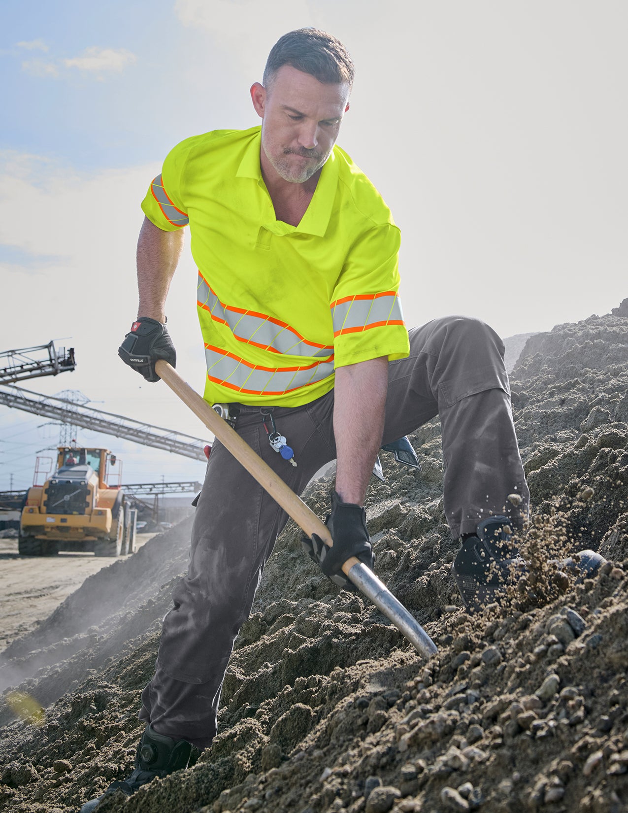 Person in high-visibility safety gear shoveling dirt on a construction site