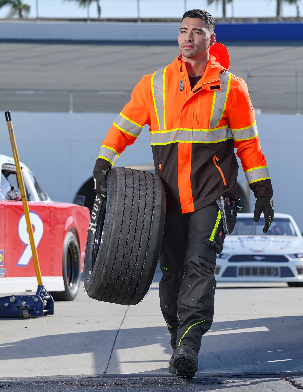Person in safety gear carrying a tire on a racetrack