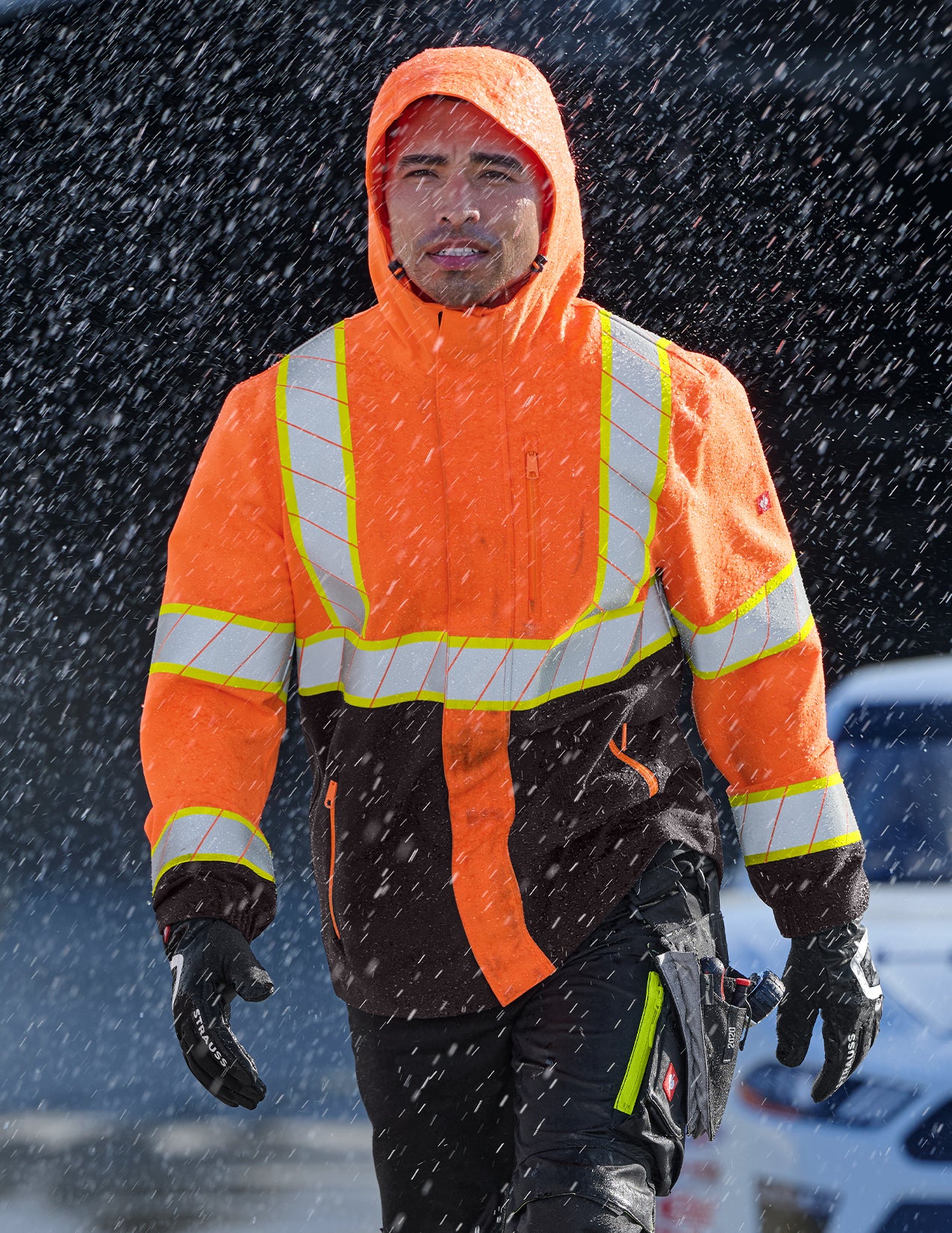 Person wearing an orange safety jacket with reflective stripes in a rainy environment