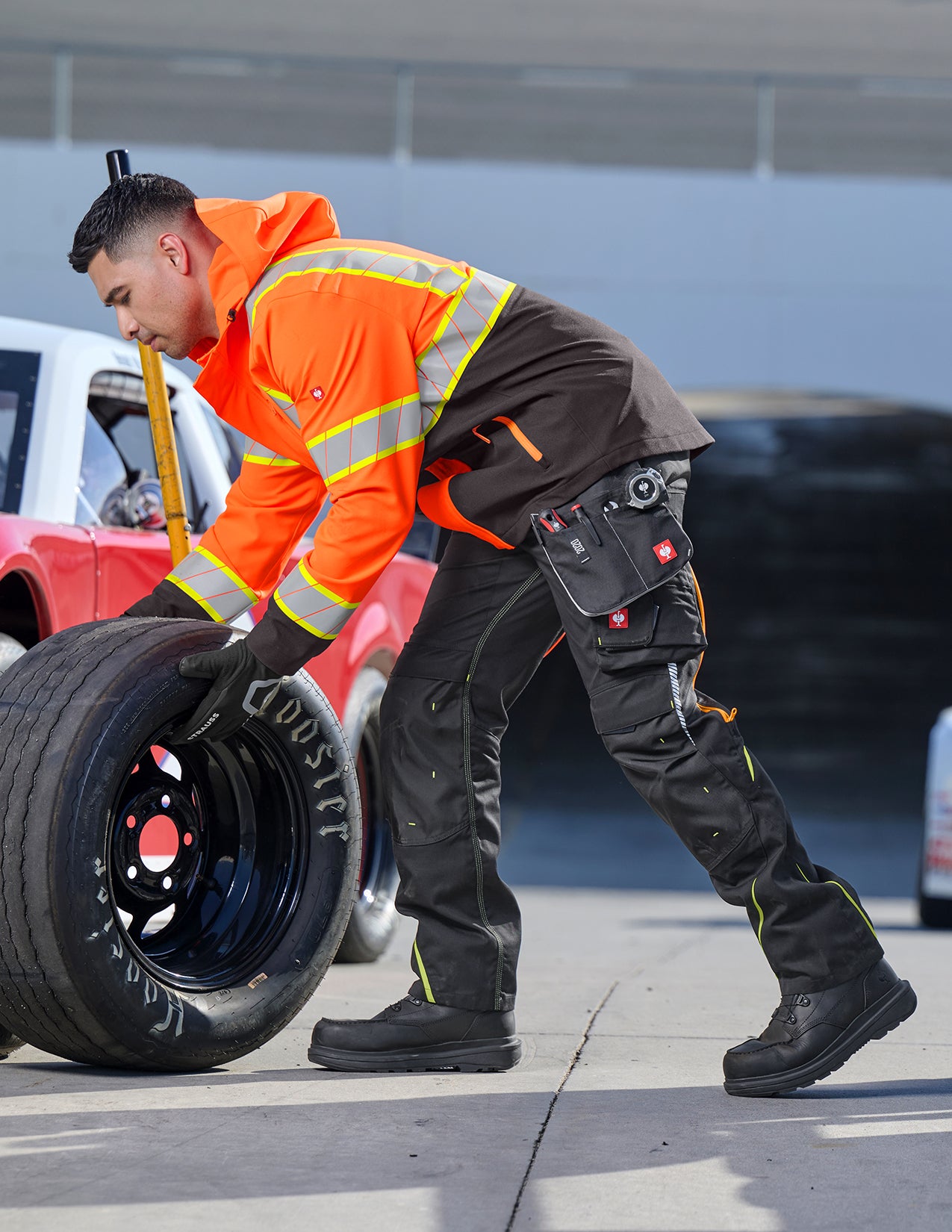 Person changing a tire on a road with a red car in the background