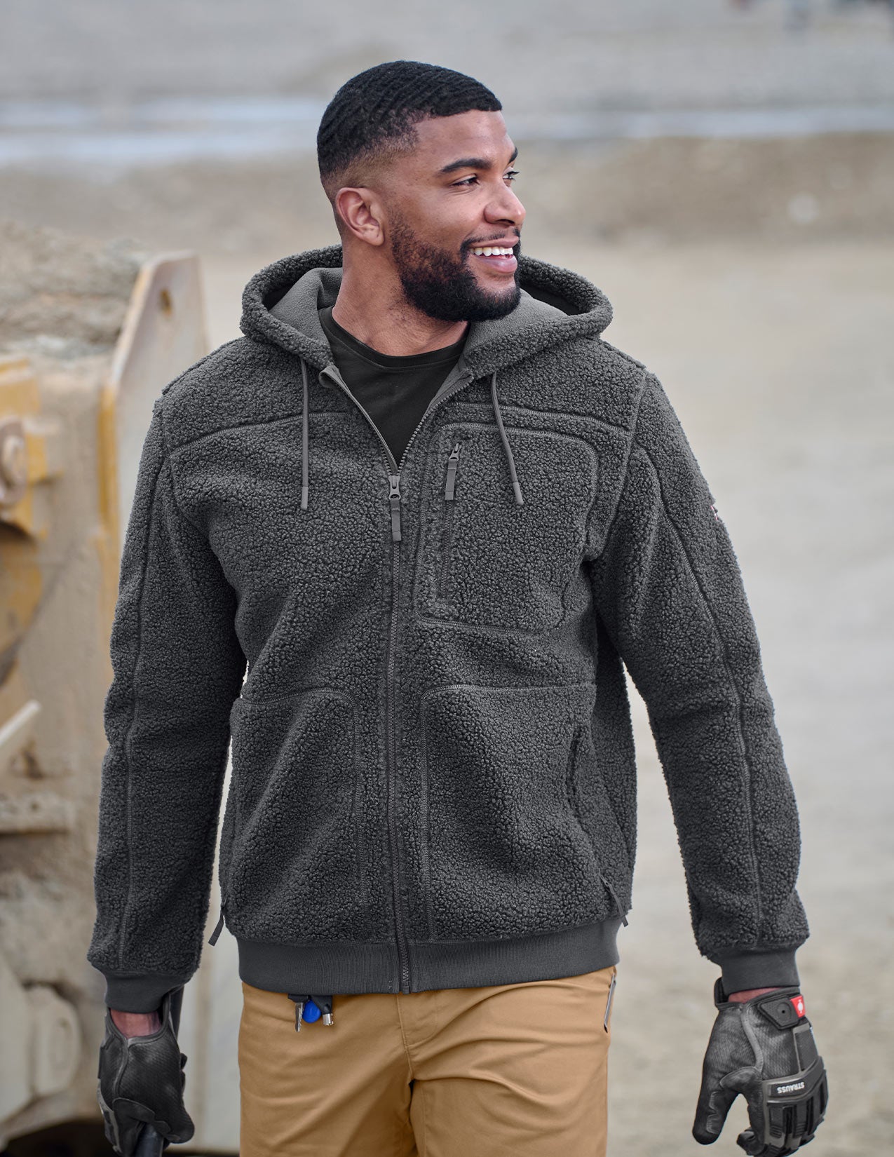 Man wearing a dark gray fleece jacket and gloves standing outdoors.
