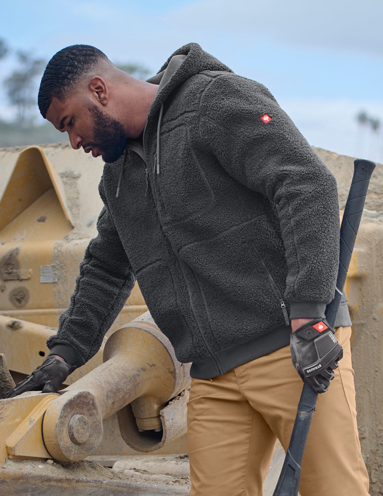 Man in a gray jacket and beige pants working on a piece of machinery.