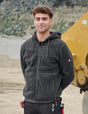 Person wearing a dark gray jacket, standing in front of a yellow piece of machinery.