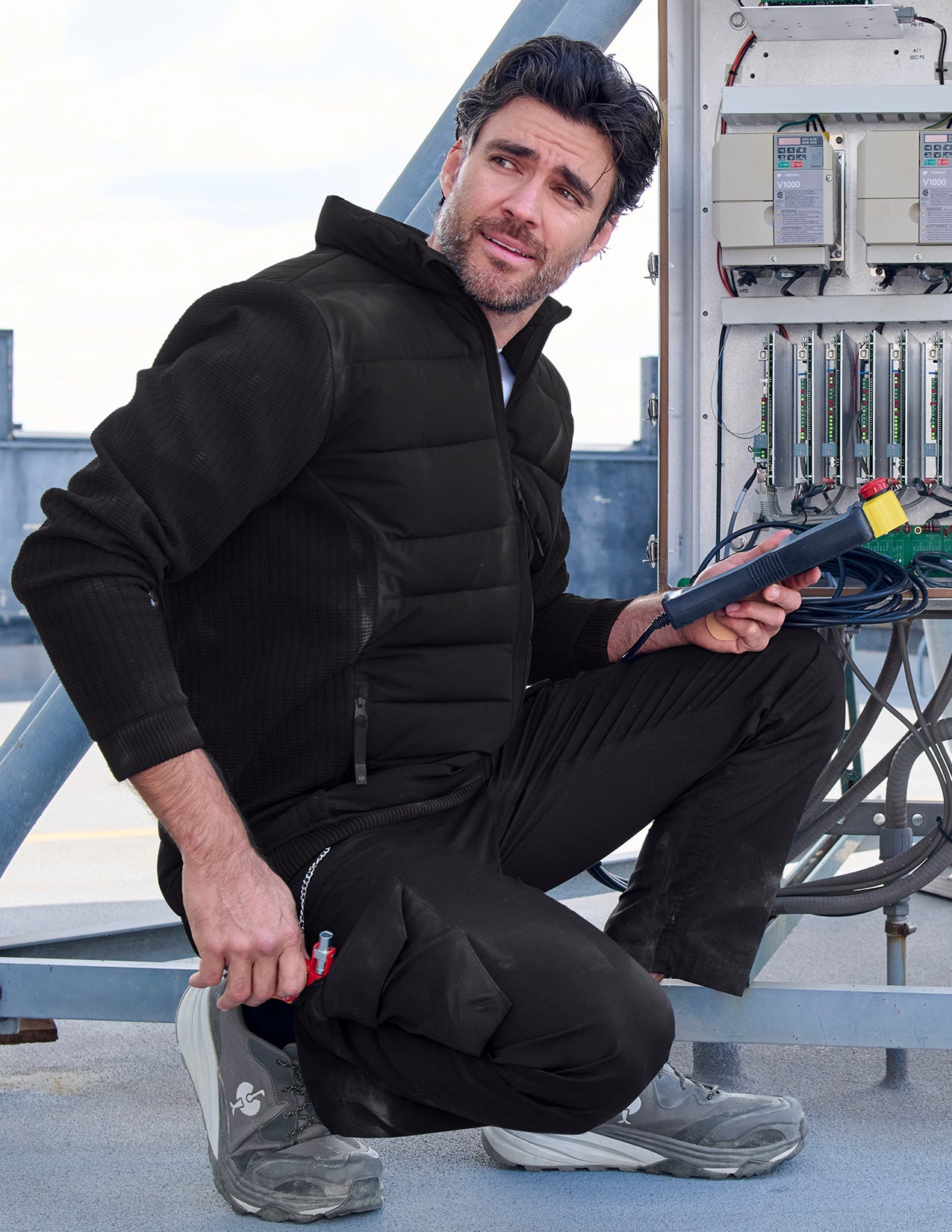 Man in black work attire sitting on a rooftop with equipment and tools.