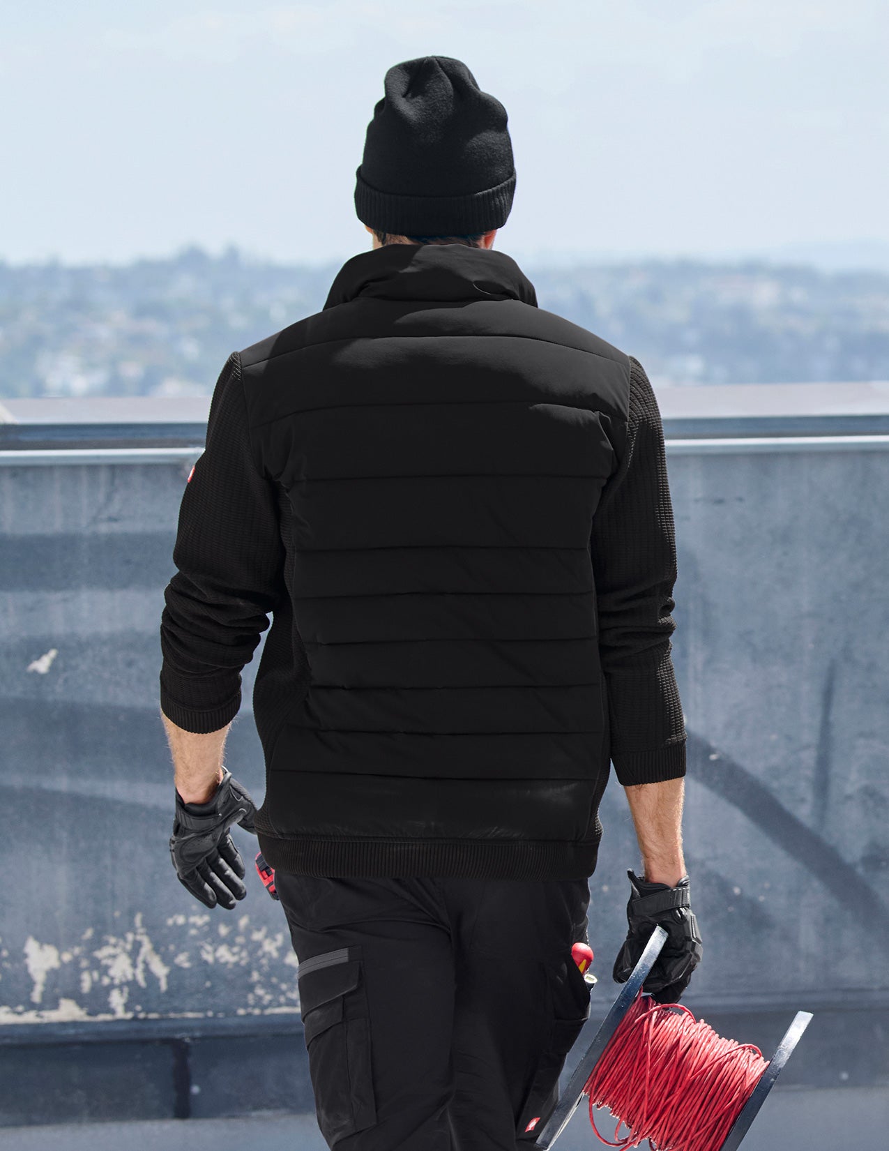 Person in black winter clothing holding red rope on a rooftop with cityscape in the background.