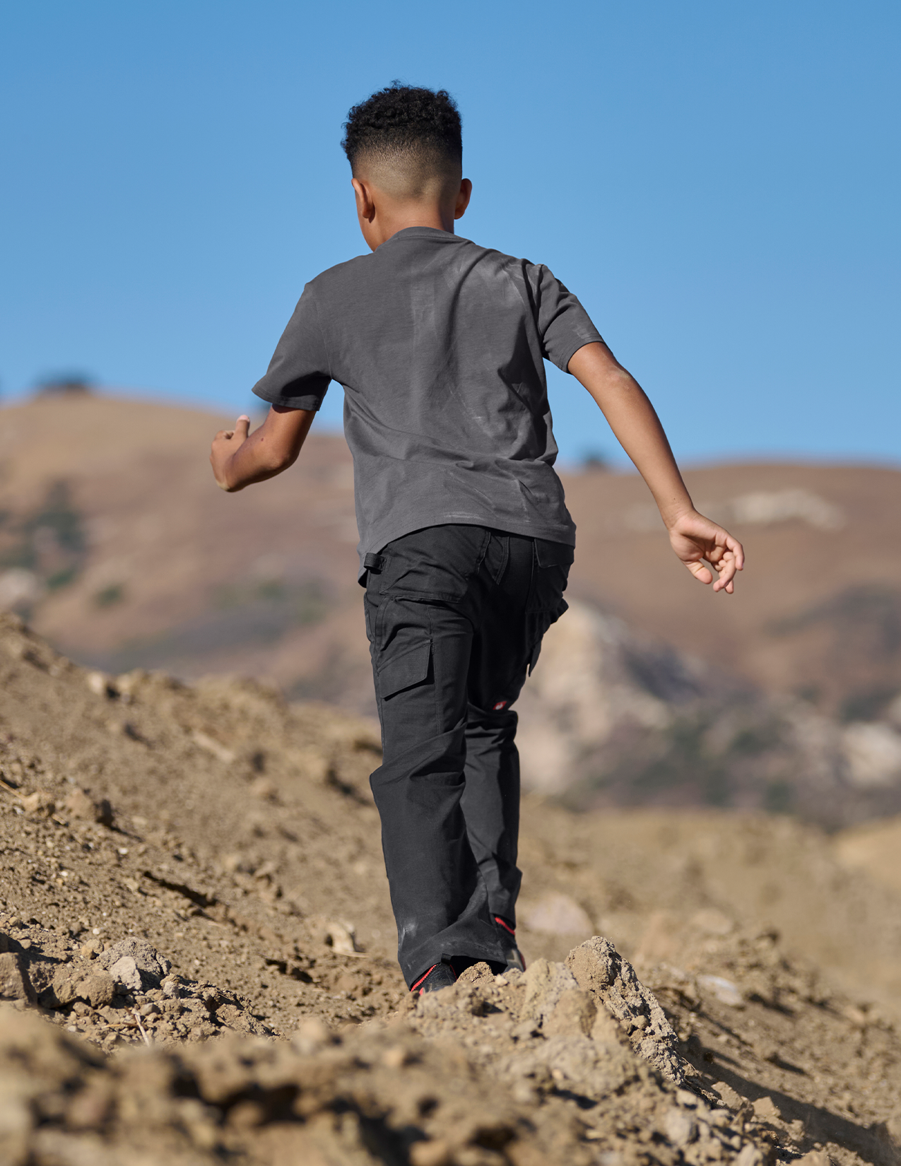 Child walking on a rocky hillside with a clear blue sky