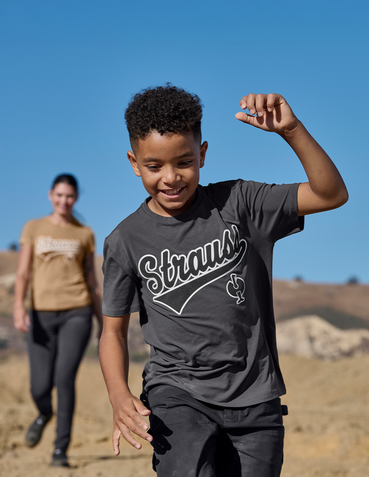 Child wearing a gray t-shirt with 'Strauss' logo outdoors