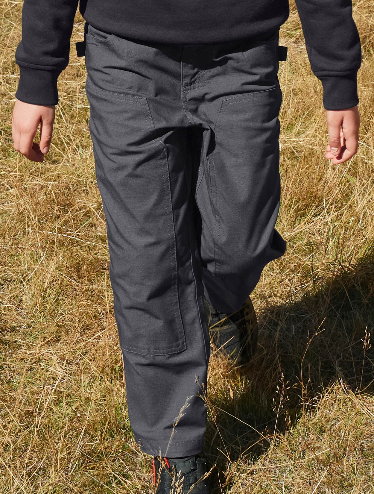 Child wearing dark pants standing in a field of dry grass