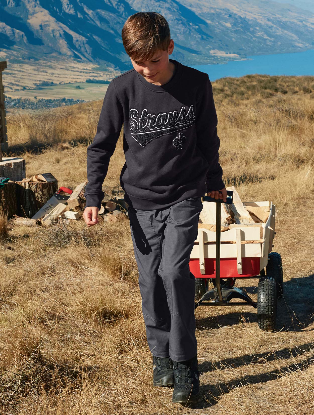 Child wearing a black 'Strauss' sweatshirt in a field with mountains in the background