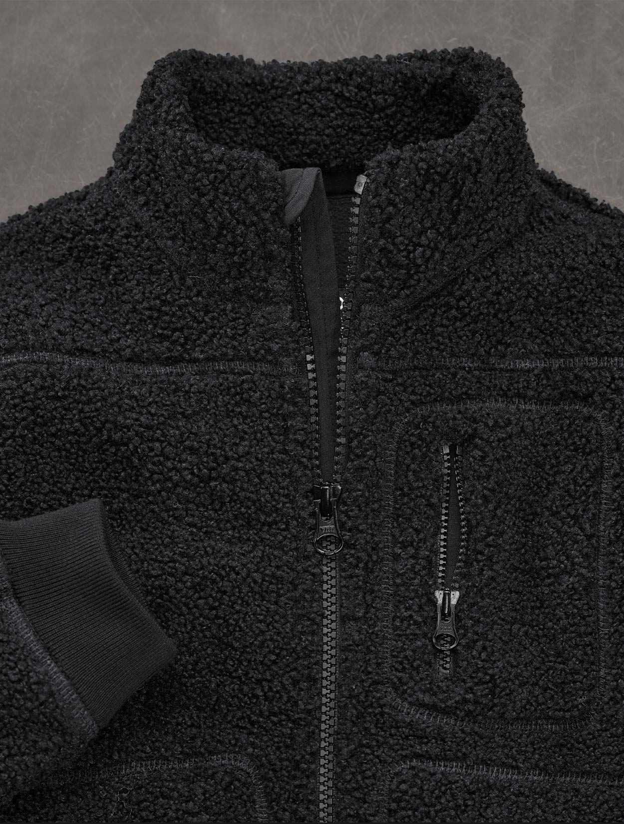 Close-up of a black fleece jacket with zippers on a gray background