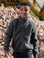 Child wearing a dark gray fleece jacket standing in front of a pile of stones.