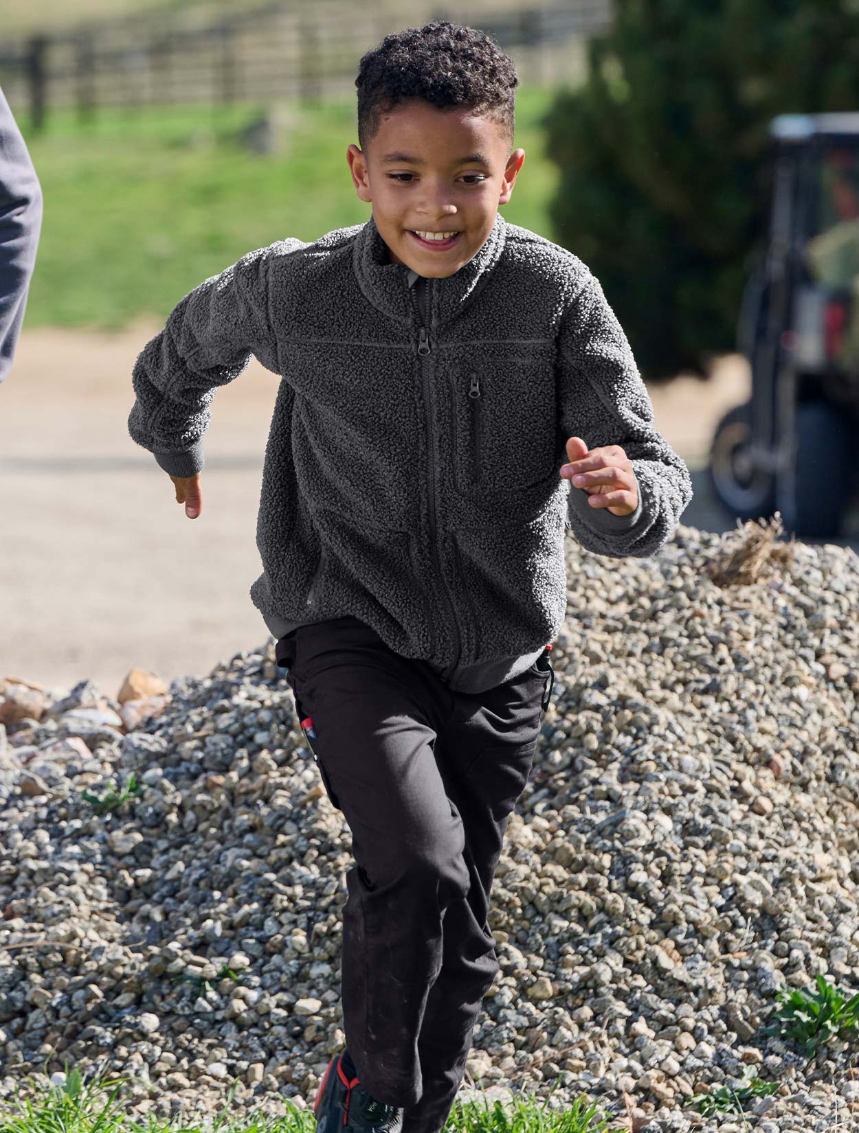 Child running outdoors on a gravel path with grass and a fence in the background