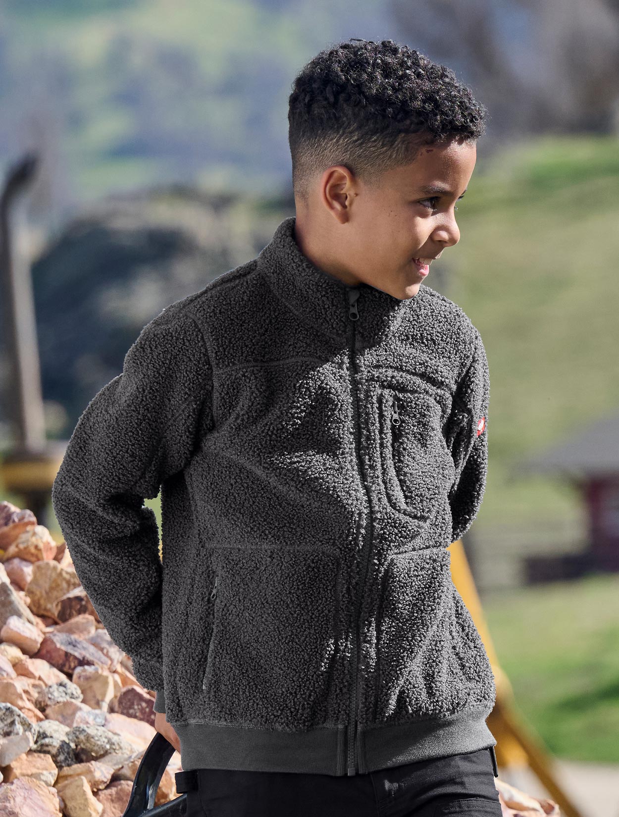 Child wearing a gray fleece jacket outdoors with a blurred natural background