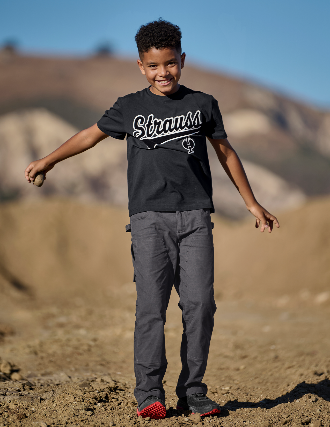 Child wearing a 'Strauss' t-shirt outdoors on a sunny day