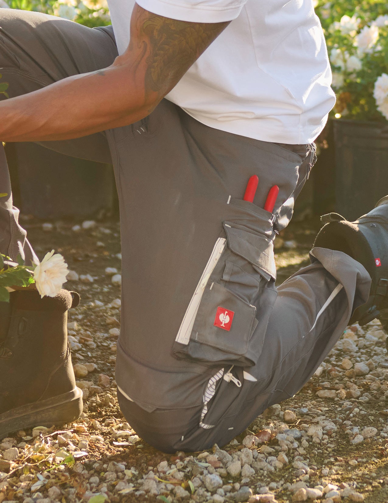 Person wearing pants with red 'Strauss' branding, standing on a rocky ground with plants in the background.