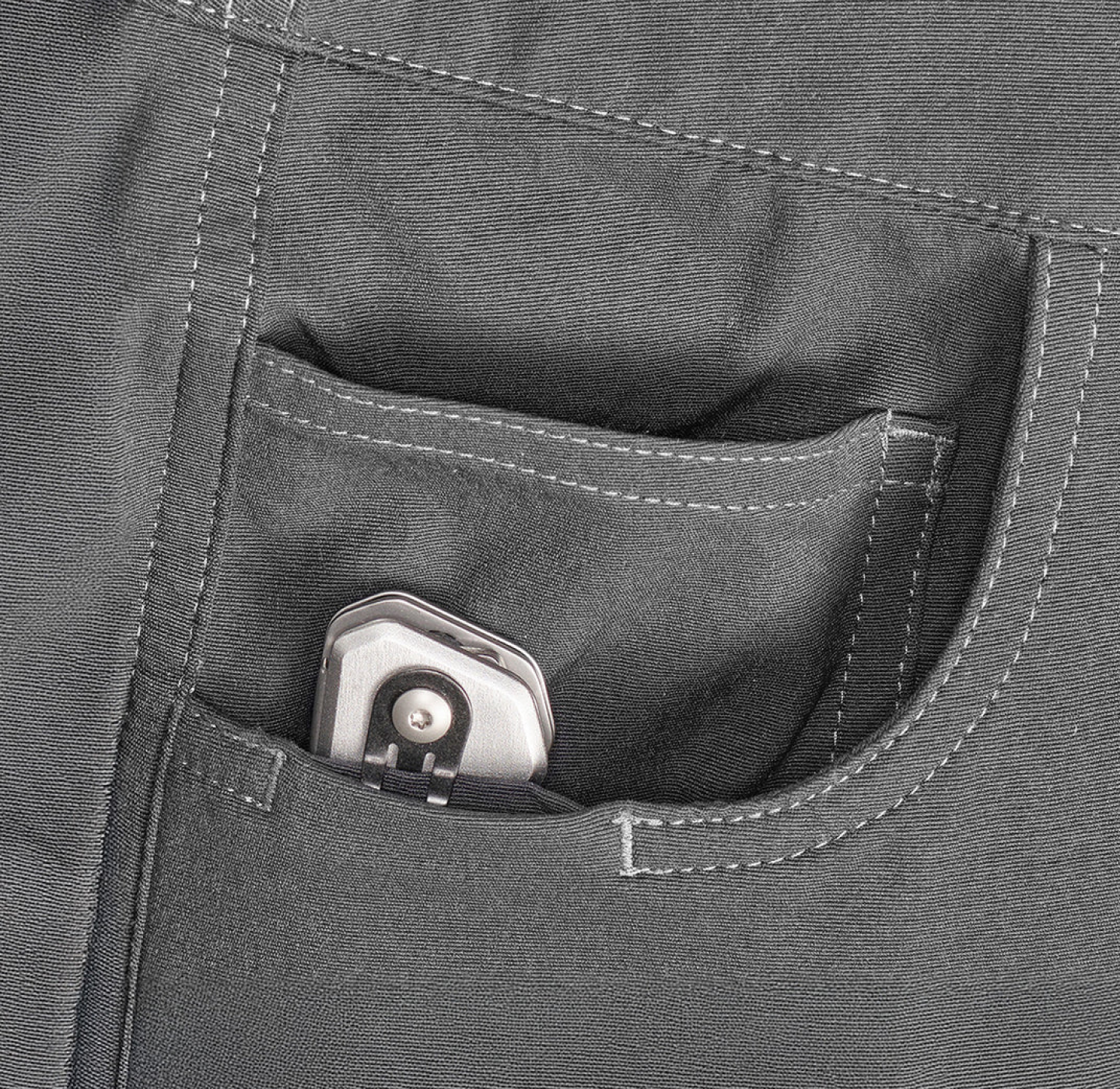 A silver folding knife partially visible inside the front pocket of gray pants.