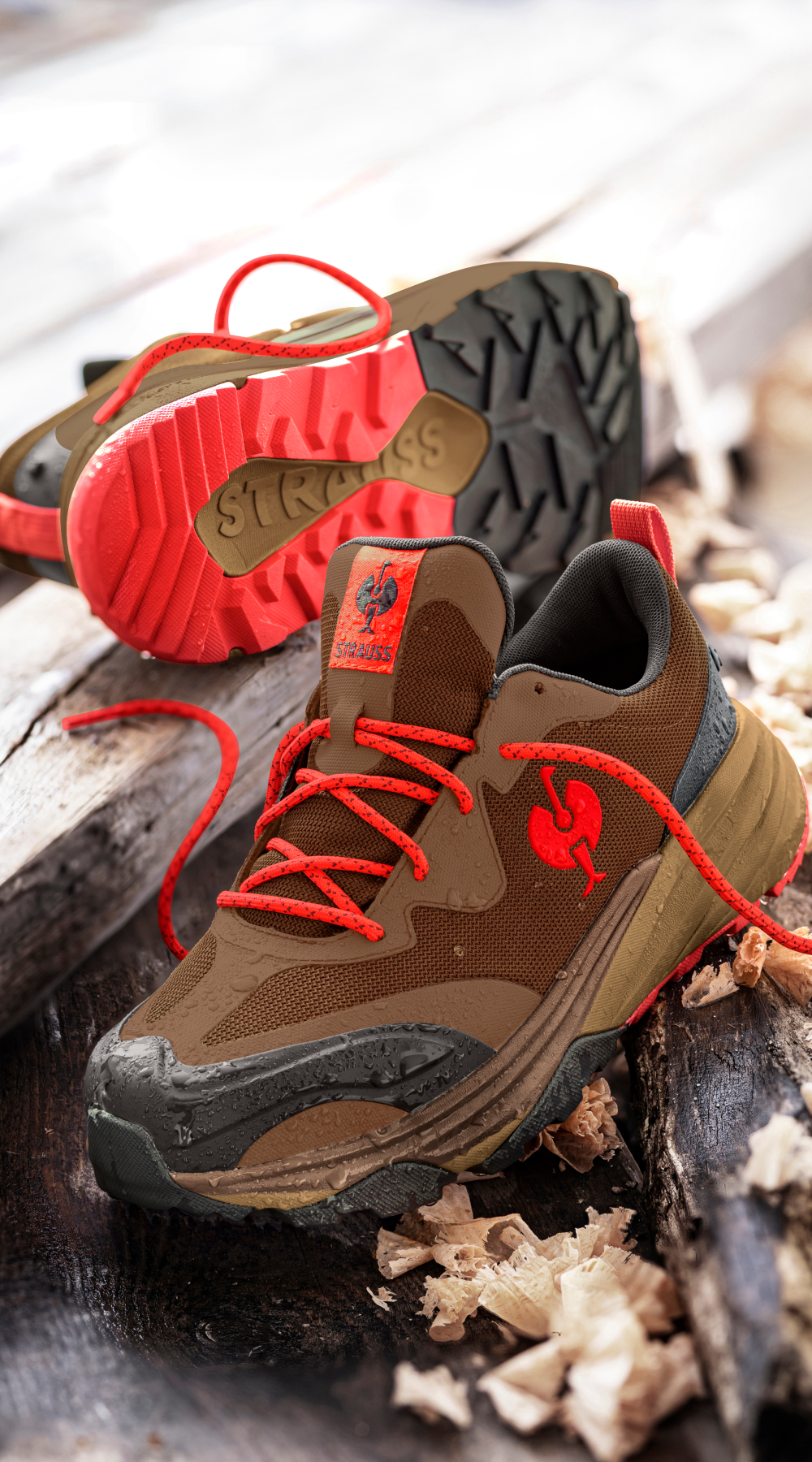 A pair of brown and red sneakers with textured soles are displayed on wooden planks, surrounded by wood shavings. One shoe is upright, and the other lies on its side, showing the sole.