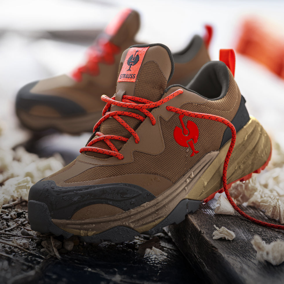Brown safey shoes in a hiking style with red laces and logo on a textured surface