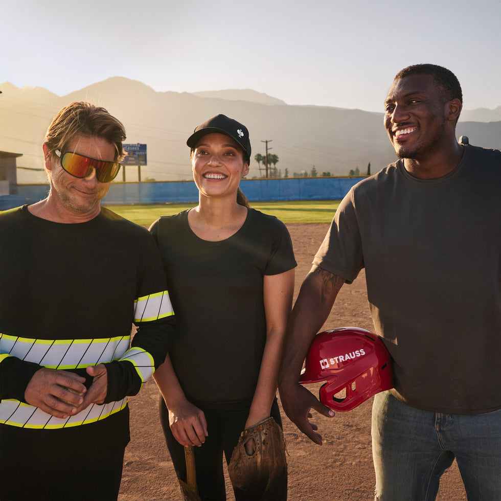 Three people standing on a baseball field with mountains in the background
