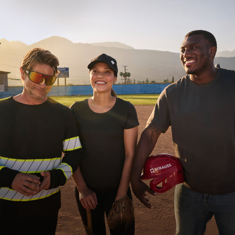 Three people play a game of pickup baseball in durable workwear with mountains in the background
