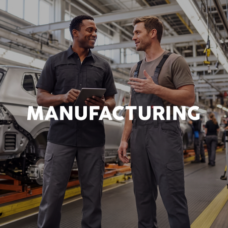 Two male manufacturing workers standing on an assembly line, one holding a tablet and the other gesturing while speaking. Large white text overlay reads 'MANUFACTURING' across the center.