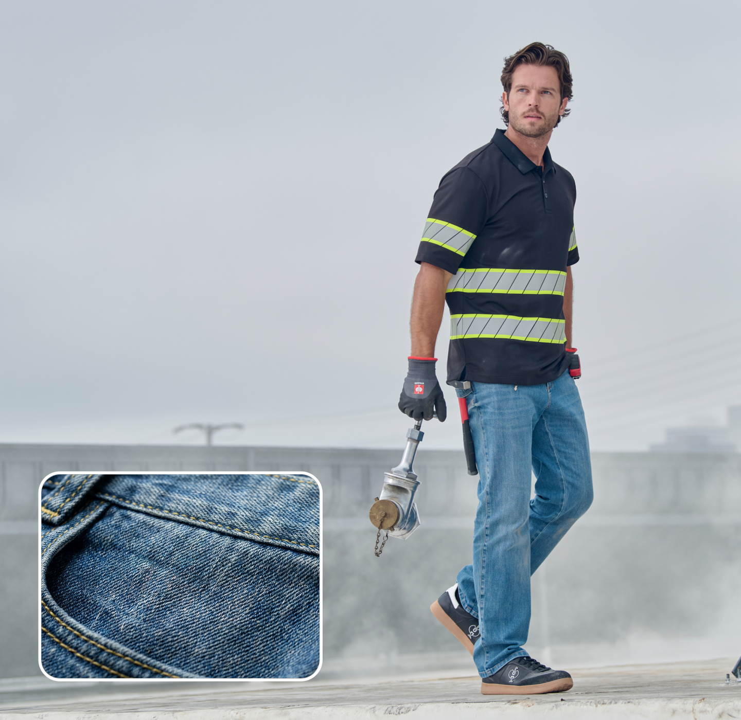 A man in jeans, gloves, and a black shirt with reflective stripes stands outdoors holding a metal tool. Inset: close-up of blue denim fabric with visible stitching. Sky and power lines are visible in the background.