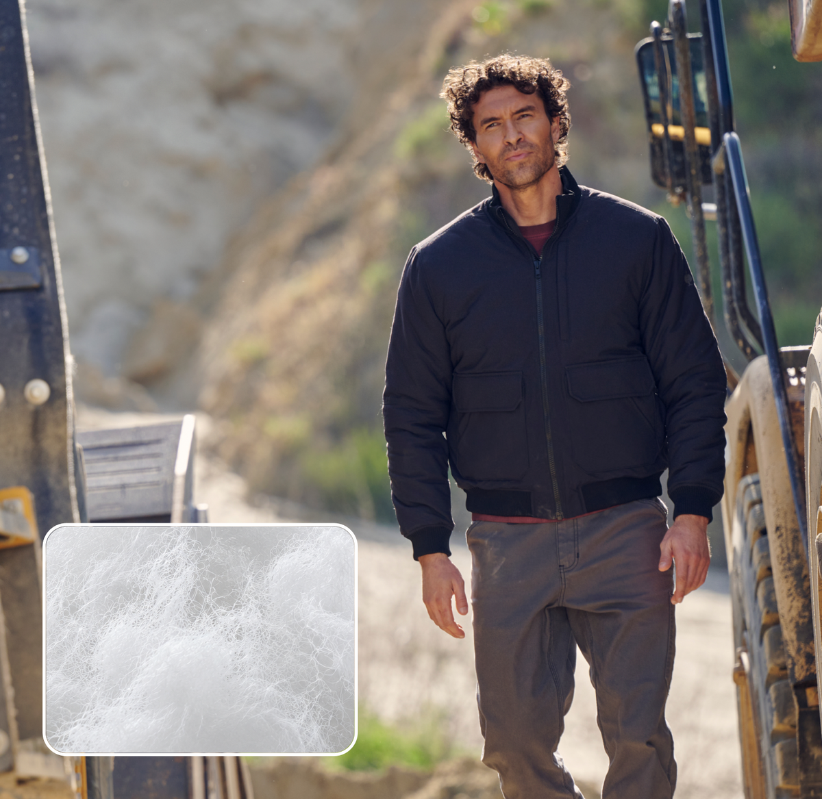 A man in a black jacket stands outdoors near construction equipment. An inset shows a close-up of the jackets inner lining.