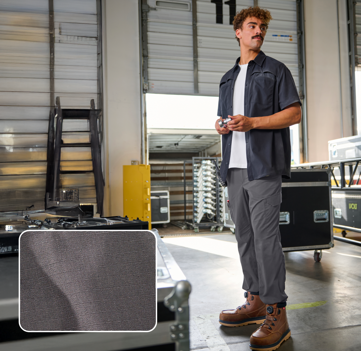 A man in work clothes and boots stands in a warehouse with equipment cases. An inset shows a close-up of the fabric texture of his gray pants.