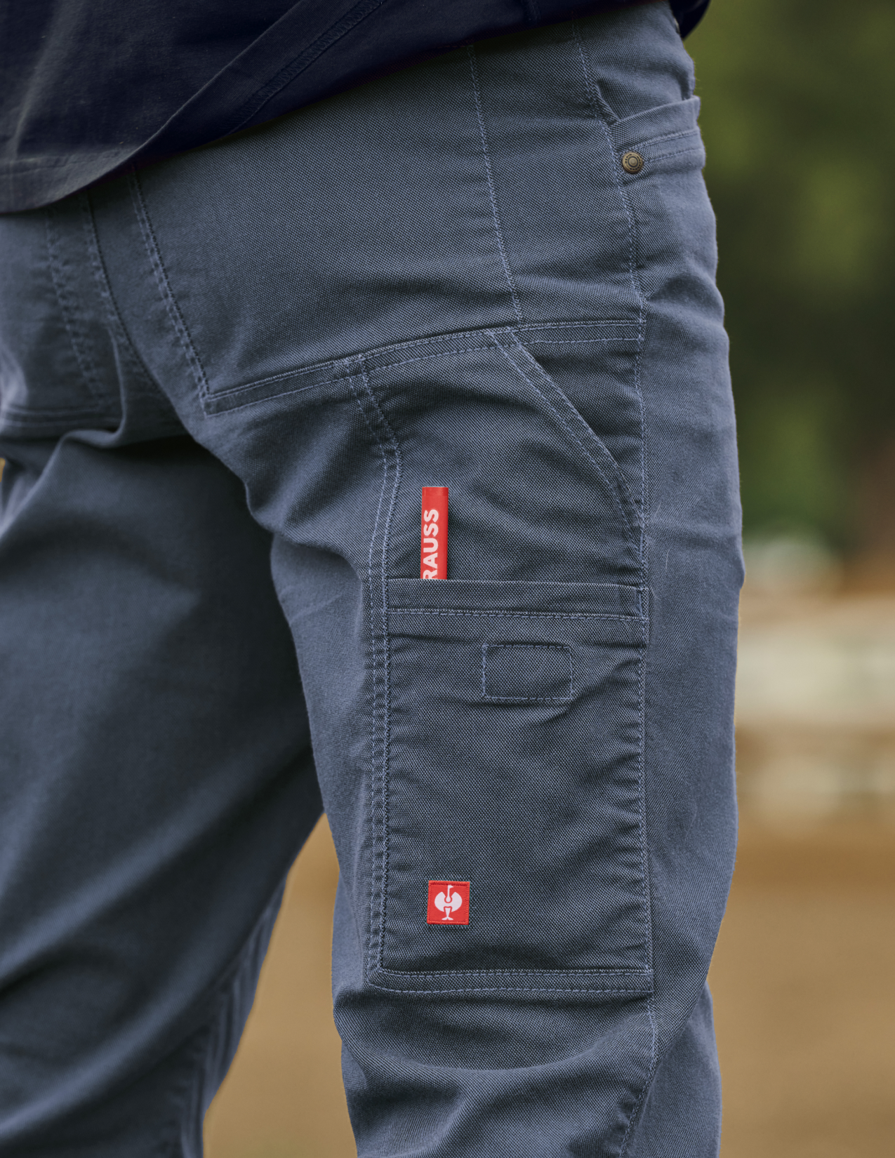 Navy cargo pants with a red label on a blurred natural background