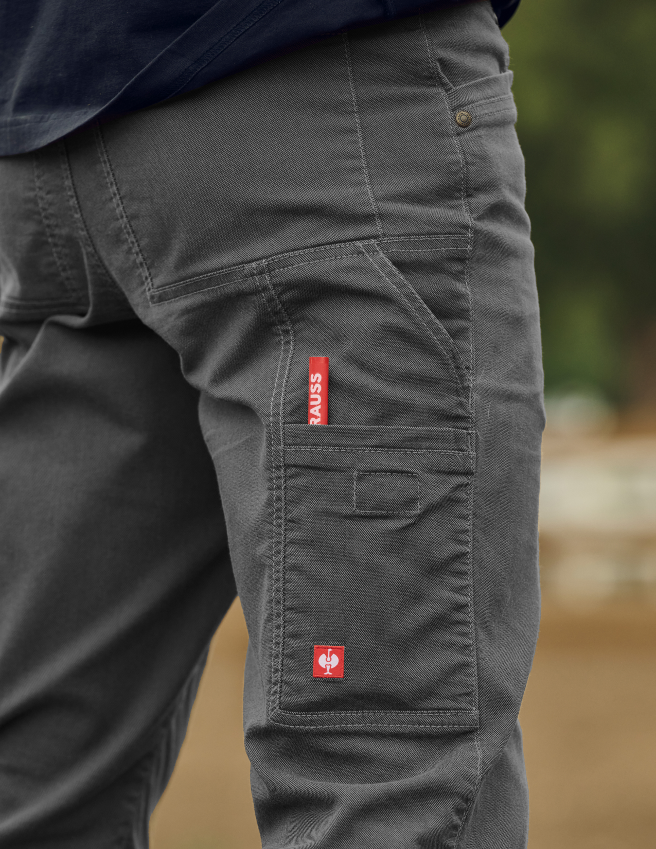 Gray cargo pants with a red and white logo on a blurred outdoor background