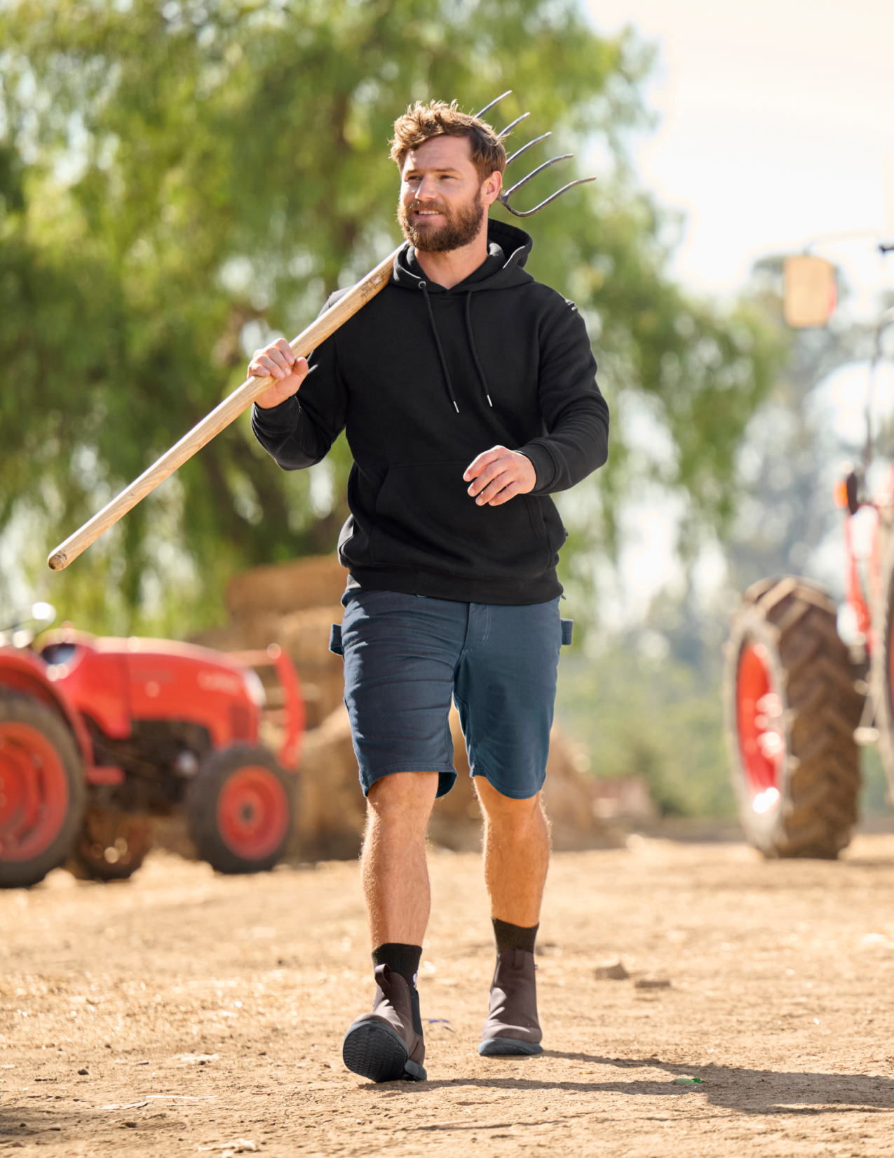 Man holding a pitchfork on a farm with tractors in the background