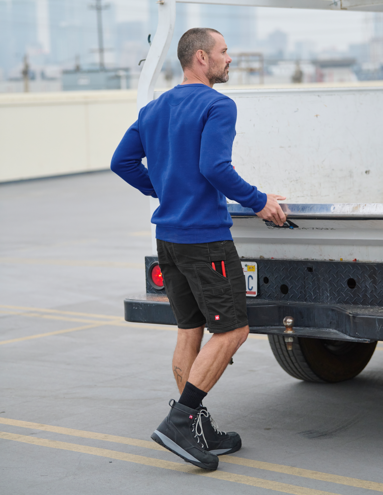 Man in blue sweatshirt and black shorts walking on a rooftop with a truck in the background