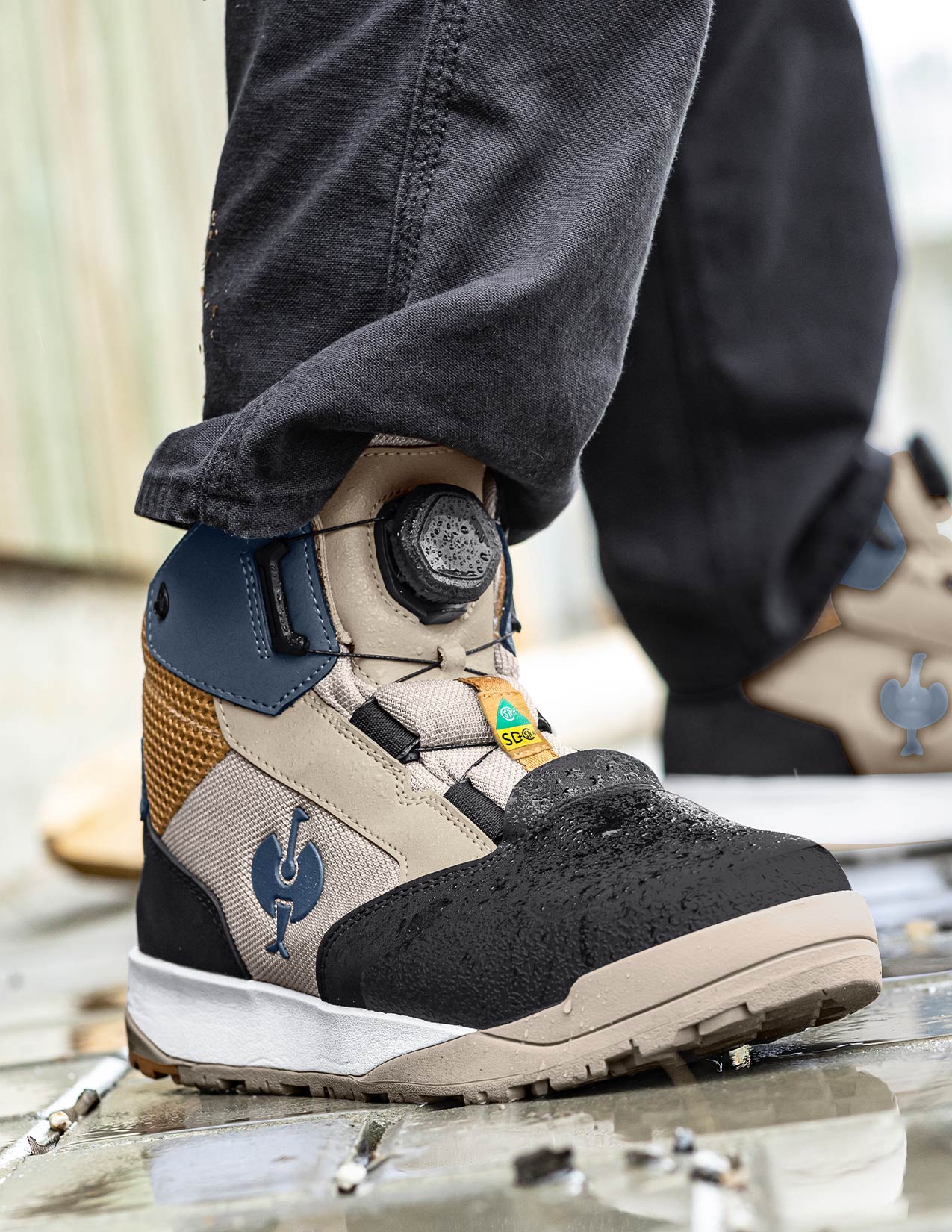 Close-up of a person wearing a work boot with visible brand logo on a blurred background