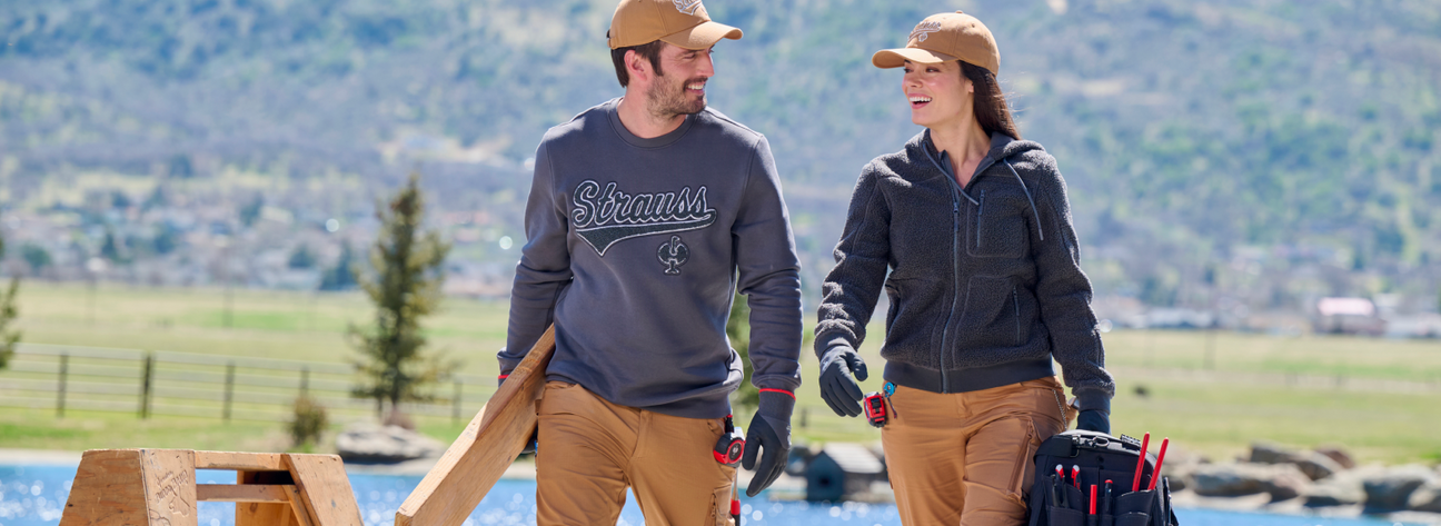 Two people walking outdoors with tools, wearing branded clothing.