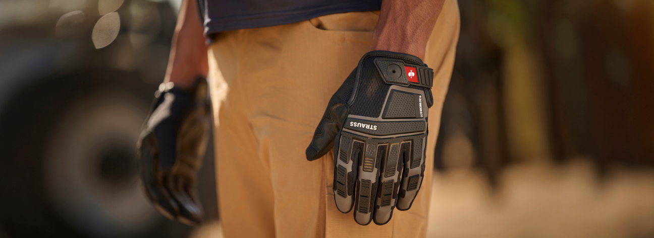A worker wearing tan cargo shorts has a black tactical work glove with red branding and protective padding on their hand.