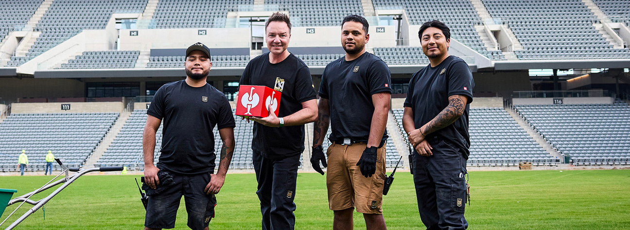 Four men standing on a sports field with a large stadium in the background