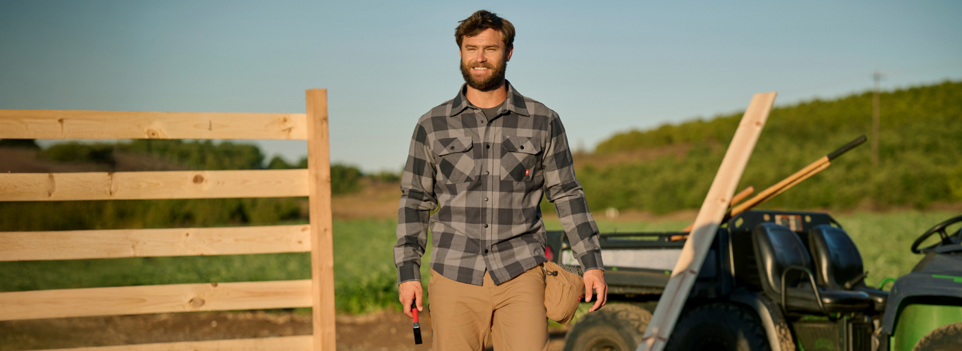 Man standing in a field with wooden planks and a truck in the background