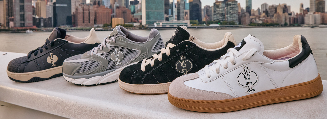 Four stylish sneakers displayed side by side against a city skyline backdrop, featuring various colors and designs.